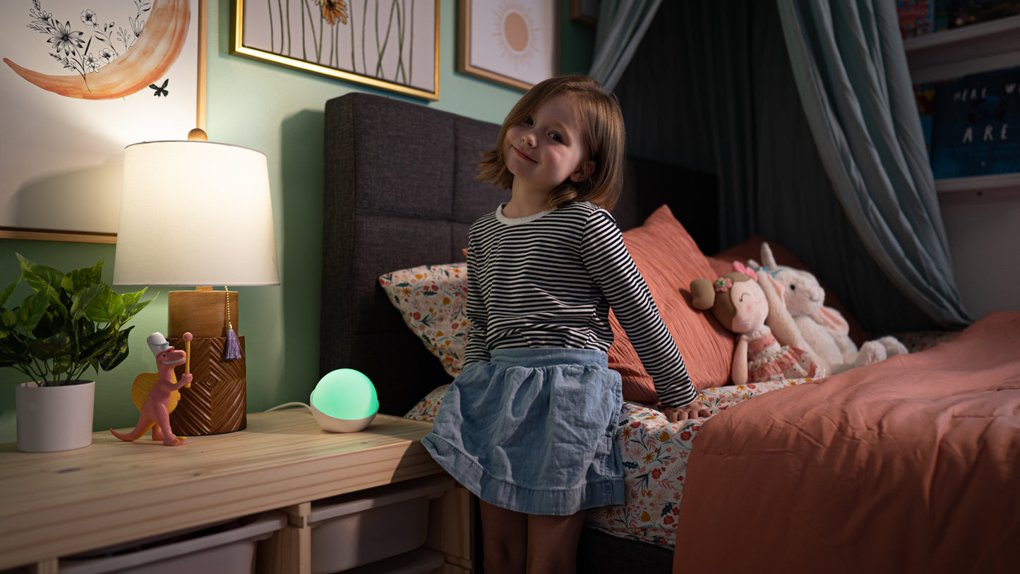 A child sitting on her bed with a Glowcose glucose monitor light beside her. It is green showing the childs type 1 diabetes is in range.